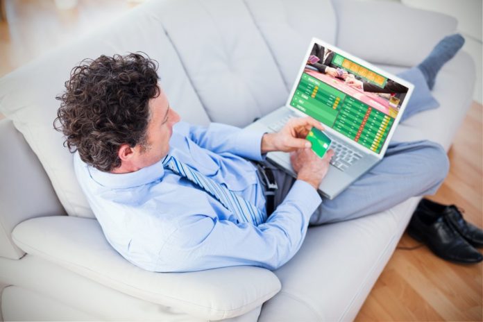 man relaxing on the couch placing a sports bet using his laptop